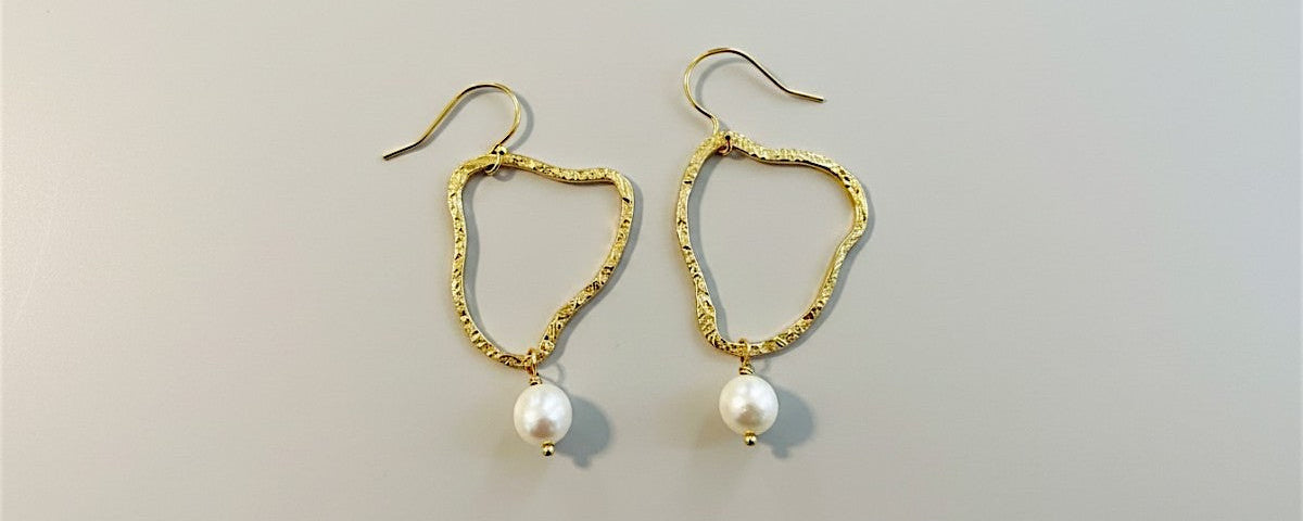 Gold earrings with pearl drops on a light gray background